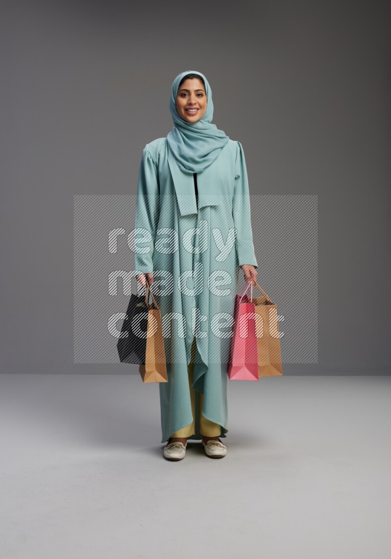 Saudi Woman wearing Abaya standing holding shopping bag on Gray background