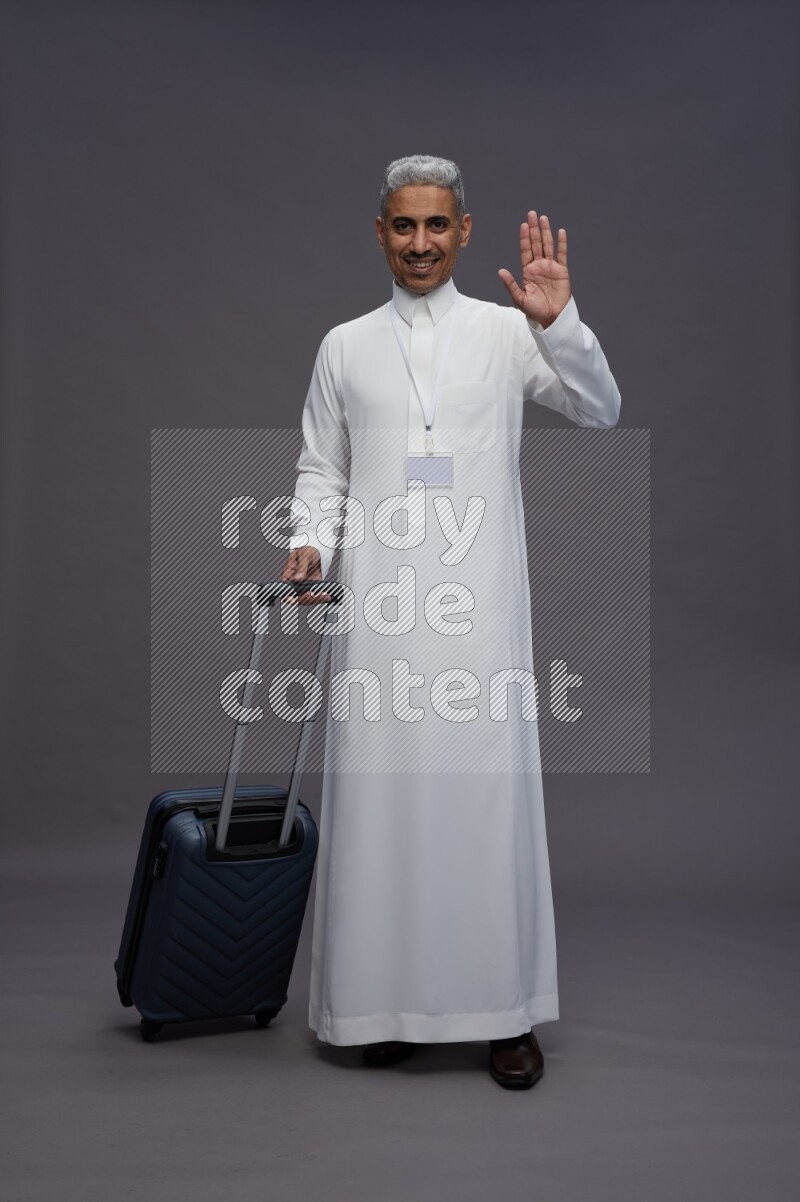 Saudi man wearing thob with neck strap employee badge standing holding bag on gray background