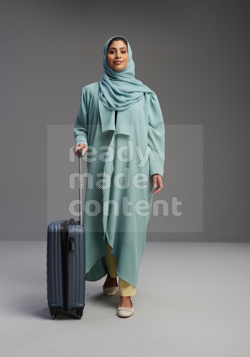 Saudi Woman wearing Abaya standing holding Travel bag on Gray background