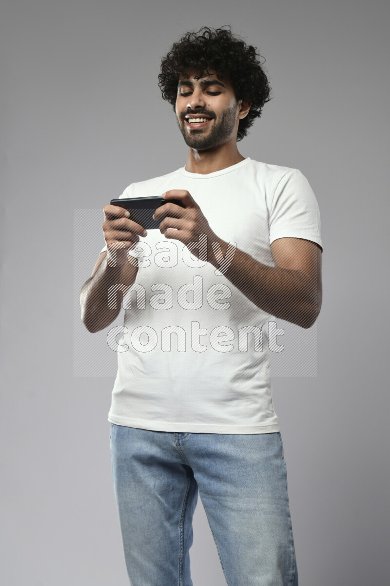 A man wearing casual standing and gaming on the phone on white background