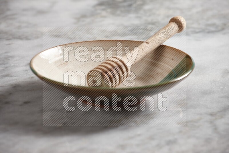 Multicolored pottery plate with wooden honey dipper in it on grey marble background