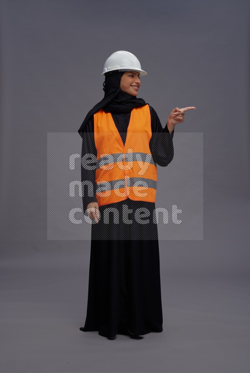 Saudi woman wearing Abaya with engineer vest standing interacting with the camera on gray background