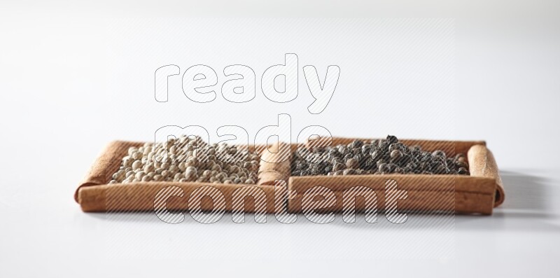 2 squares of cinnamon sticks full of black pepper and white pepper on white flooring