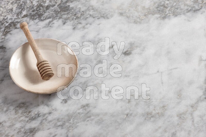 Beige pottery plate with wooden honey dipper in it on grey marble background