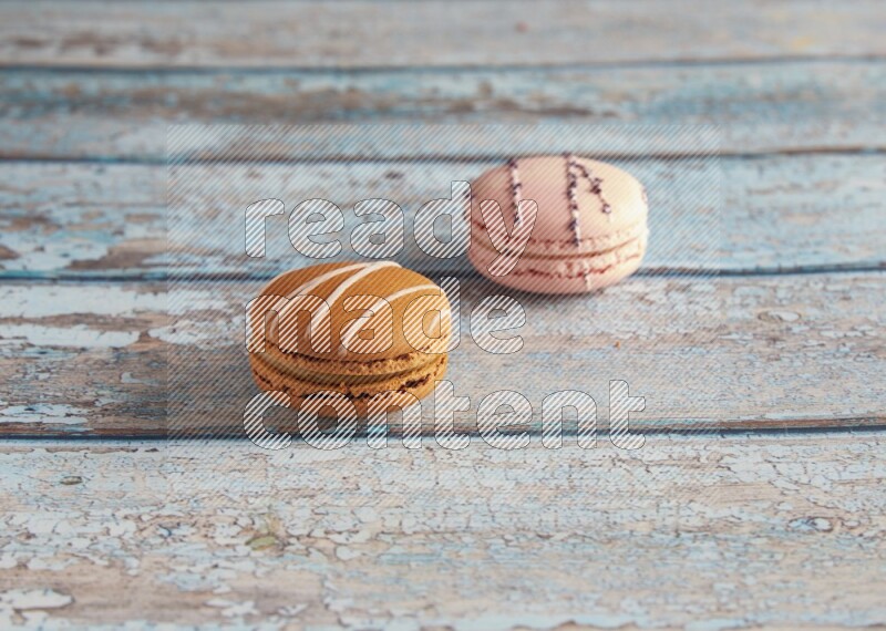 45º Shot of of two assorted Brown Irish Cream, and pink orange blossom  macarons on light blue background
