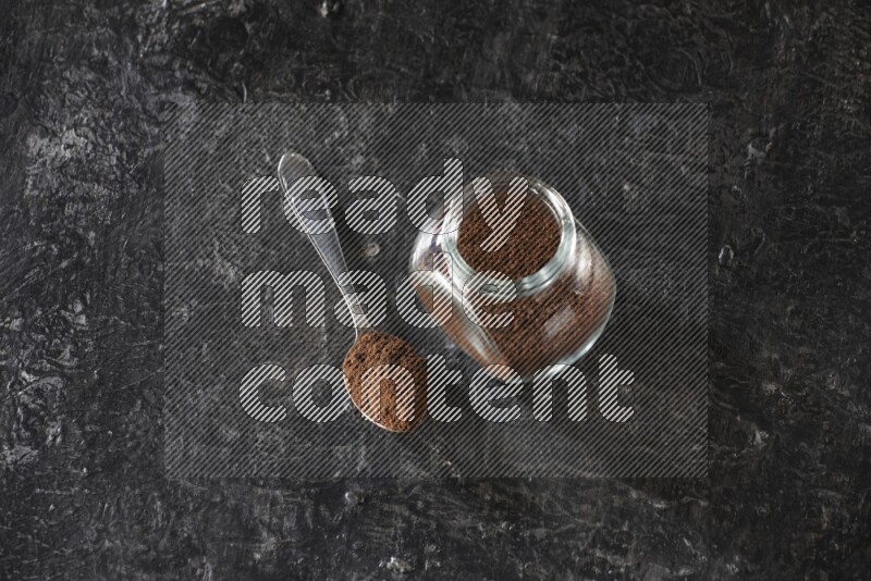 وعاء زجاجي للبهارات وملعقة معدنية ممتلئان ببودرة القرنفل على أرضية سوداء