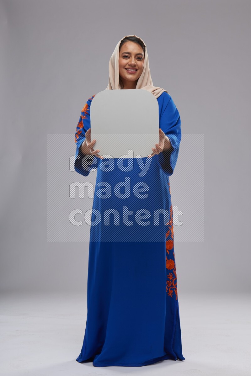 A Saudi woman standing wearing Jalabeya holding a social media sign