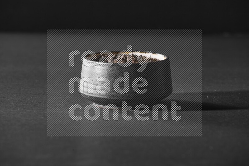 حبوب الفلفل الأسود في وعاء فخاري أسود علي خلفية سوداء