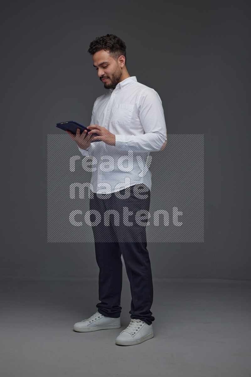 A man wearing smart casual standing and using his tablet eye level on a gray background