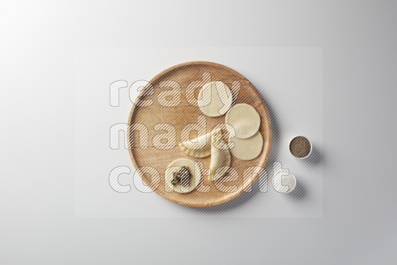 two closed sambosas and one open sambosa filled with meat while salt and black pepper aside in a wooden dish on a white background