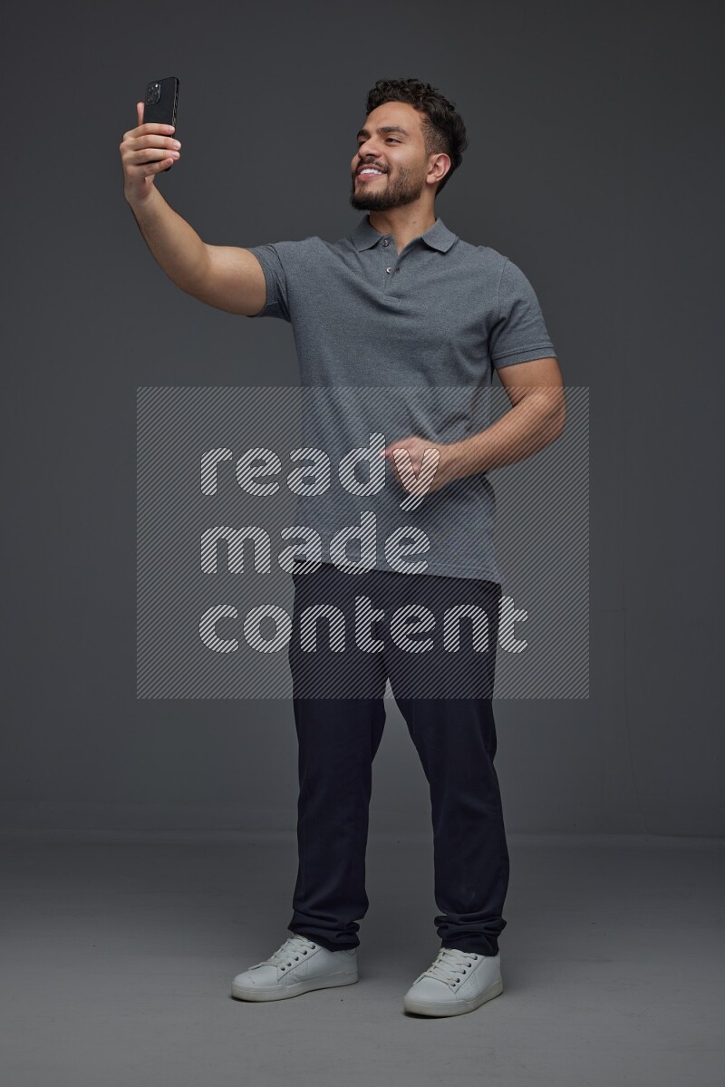 A man wearing casual and taking selfie with his phone different angles eye level on a gray background