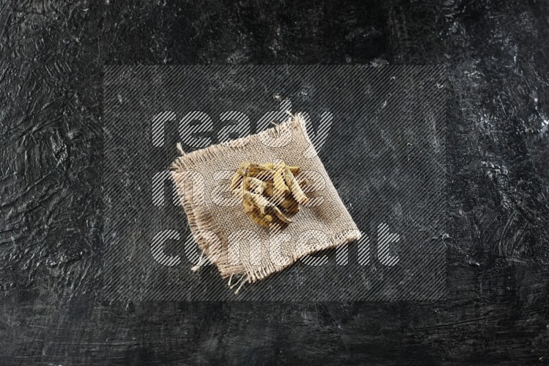 Dried turmeric whole fingers on a burlap piece of fabric on textured black flooring