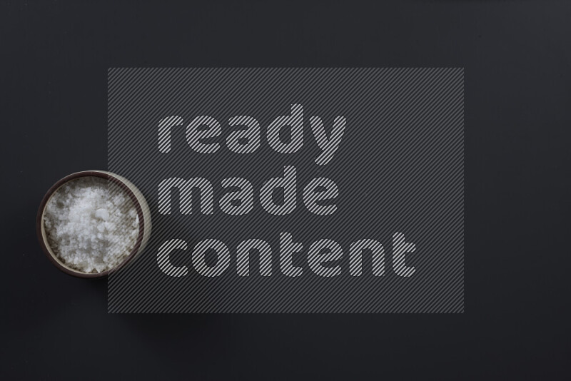 وعاء فخاري ممتلئ بملح الطعام الناعم وملح البحر الخشن على خلفية سوداء