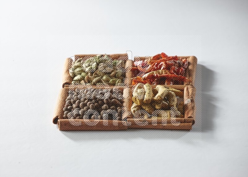 4 مربعات من أعواد القرفة ممتلئة بالفلفل الأحمر المجفف والهيل وأصابع الكركم وبهار الفلفل الحلو على أرضية بيضاء