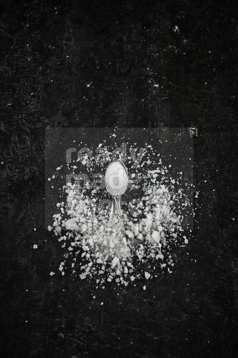2 metal spoons filled with white salt on black background