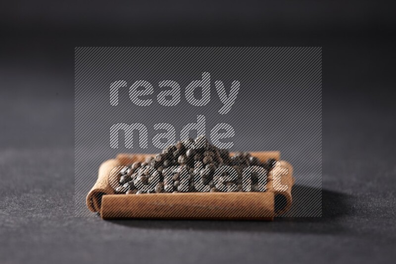 A single square of cinnamon sticks full of black pepper on black flooring