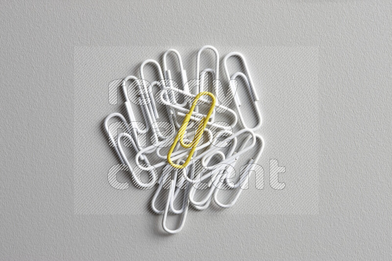A bunch of white paper clips with a different colored paper clip in the center on grey background