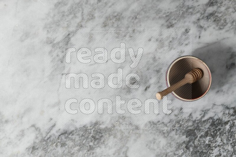 وعاء فخاري بيج مع ملعقة عسل خشبية بداخله على خلفية من الرخام الرمادي