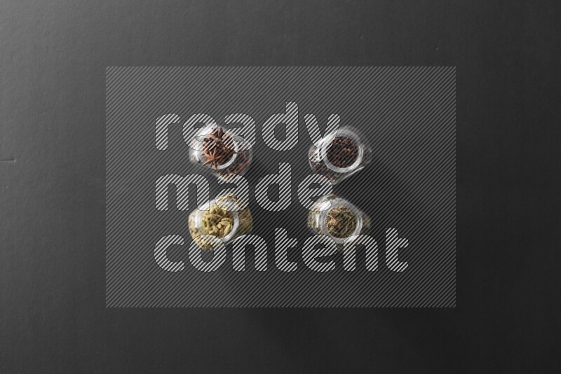 قرنفل وحبوب الهيل وريحان مجفف ويانسون نجمي في أوعية زجاجية علي خلفية سوداء