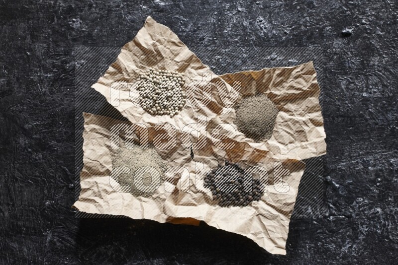 Crumpled pieces of paper full of black and white pepper beads and powder on a textured black flooring