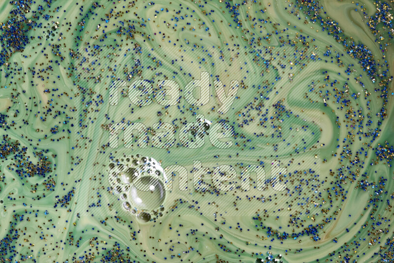 A close-up of sparkling blue and gold glitter scattered on swirling green background