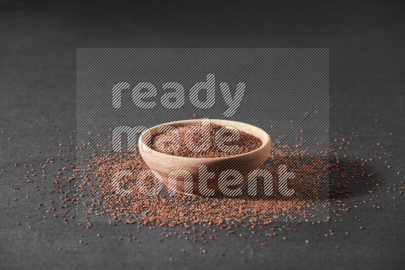 وعاء خشبي ممتلئ ببذور حب الرشاد محاط ببعض البذور علي خلفية سوداء