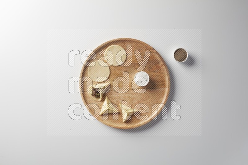 two closed sambosas and one open sambosa filled with meat while salt and black pepper aside in a wooden dish on a white background