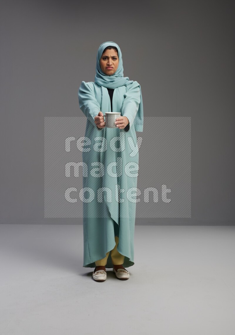 Saudi Woman wearing Abaya standing  holding a mug on Gray background