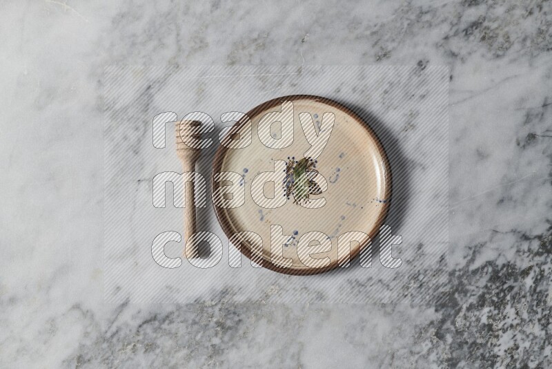 Decorative pottery plate with wooden honey dipper on the side on grey marble background
