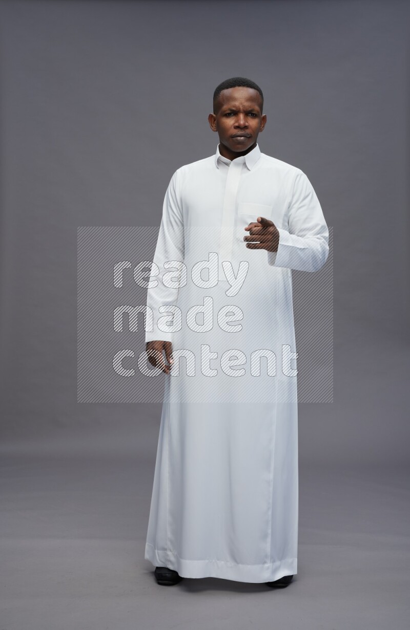 Saudi man wearing thob standing interacting with the camera on gray background