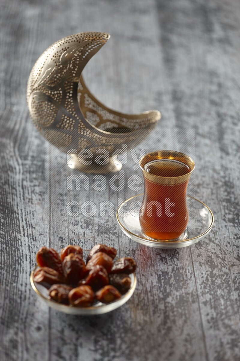 A silver lantern with different drinks, dates, nuts, prayer beads and quran on grey wooden background