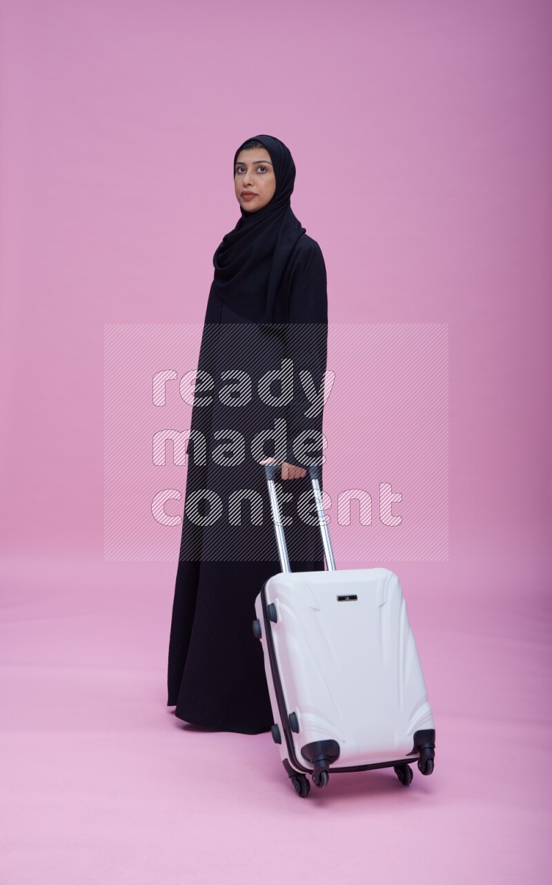 Saudi woman wearing Abaya standing holding bag on pink background