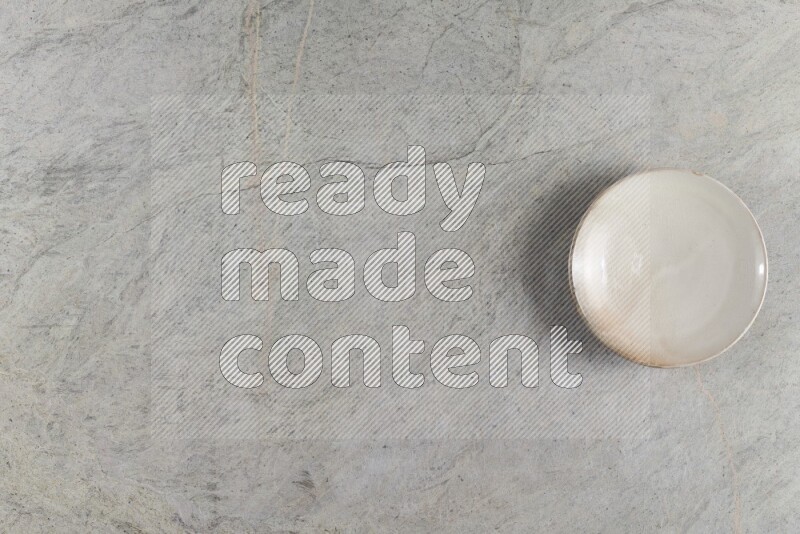 A circular beige pottery plate on grey marble background