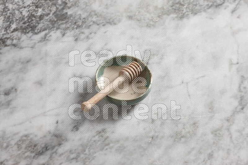 Multicolored pottery bowl with wooden honey dipper in it on grey marble background