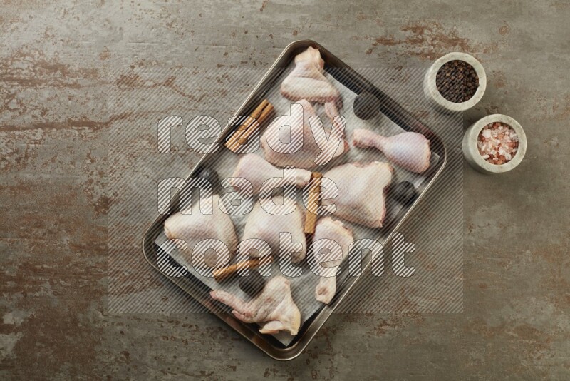 Mixed fresh chicken pieces in an oven tray on a textured rustic background