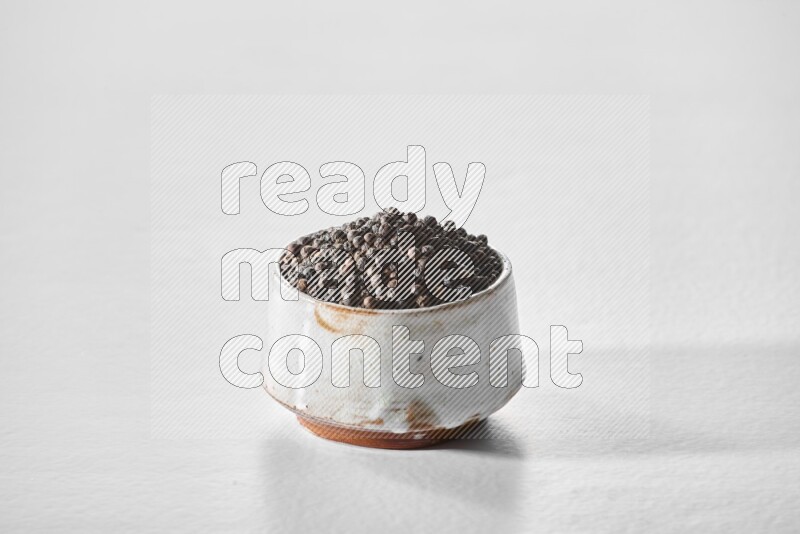 A white ceramic bowl full of black pepper on white flooring