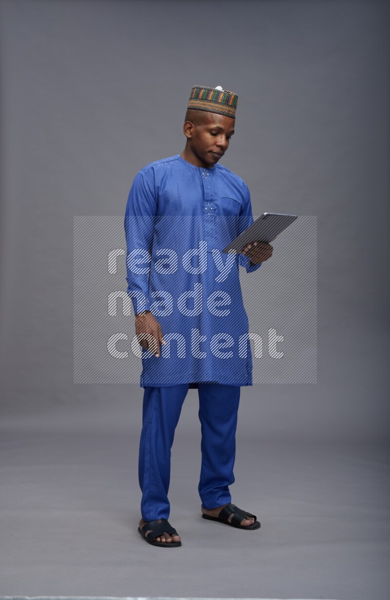 Man wearing Nigerian outfit standing working on tablet on gray background