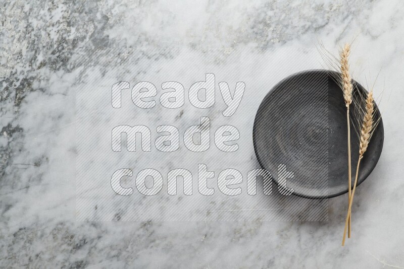 Wheat stalks on black pottery plate on grey marble background