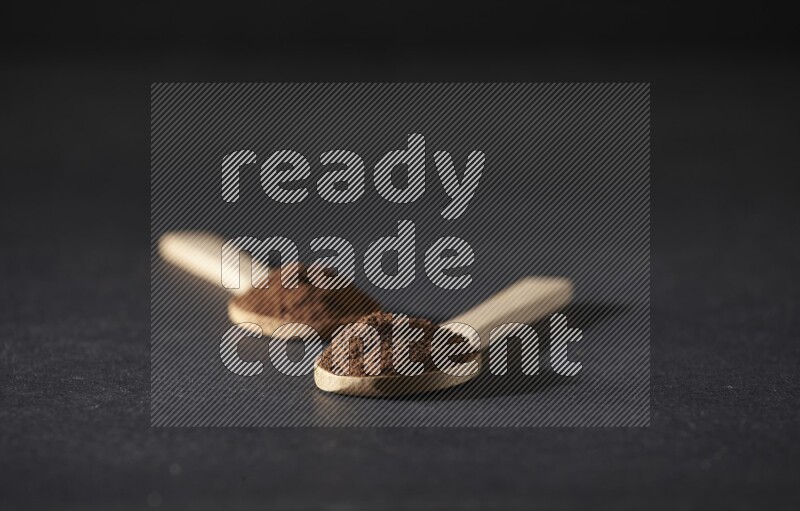 ملعقتان خشبيتان ممتلئتان ببودرة القرنفل على خلفية سوداء