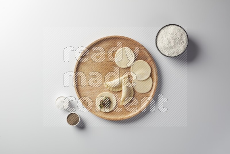 two closed sambosas and one open sambosa filled with meat while flour, salt, and black pepper aside in a wooden dish on a white background