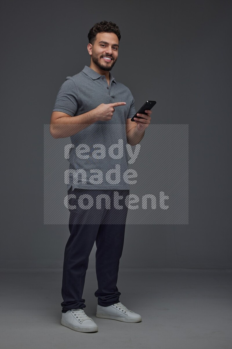 A man wearing casual standing and using his phone and making multi hand gestures eye level on a gray background
