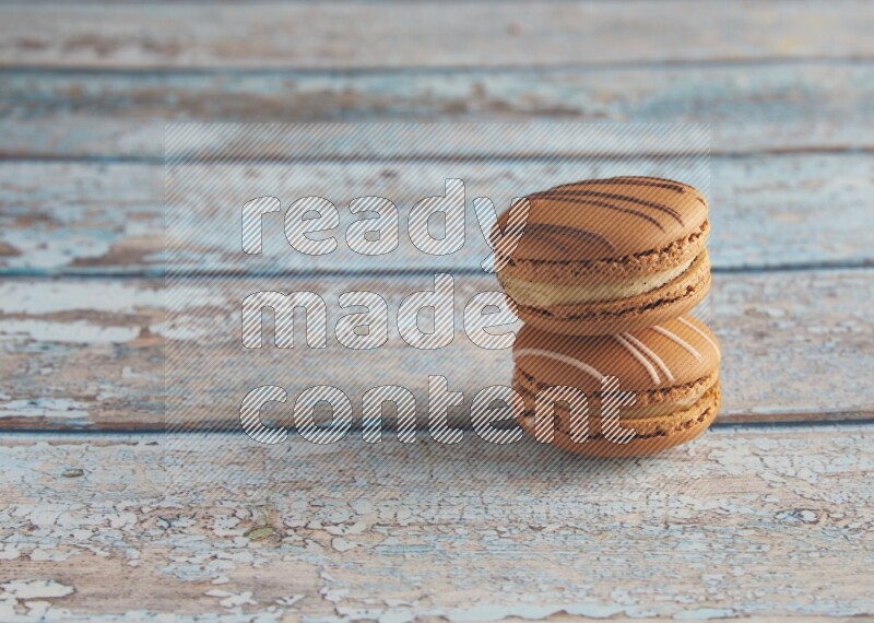 45º Shot of of two assorted Brown Irish Cream, and light brown Almond Cream macarons next to each other on light blue background