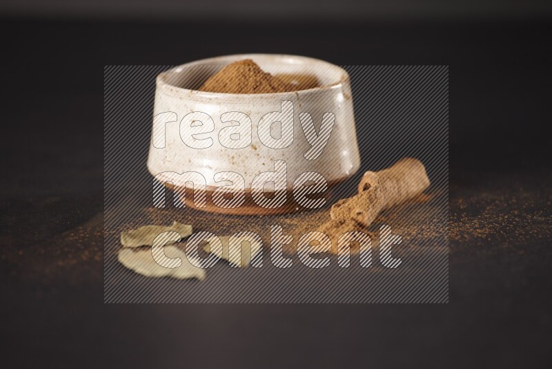 Cinnamon powder in a white pottery bowl and cinnamon sticks and laurel leaves on black background