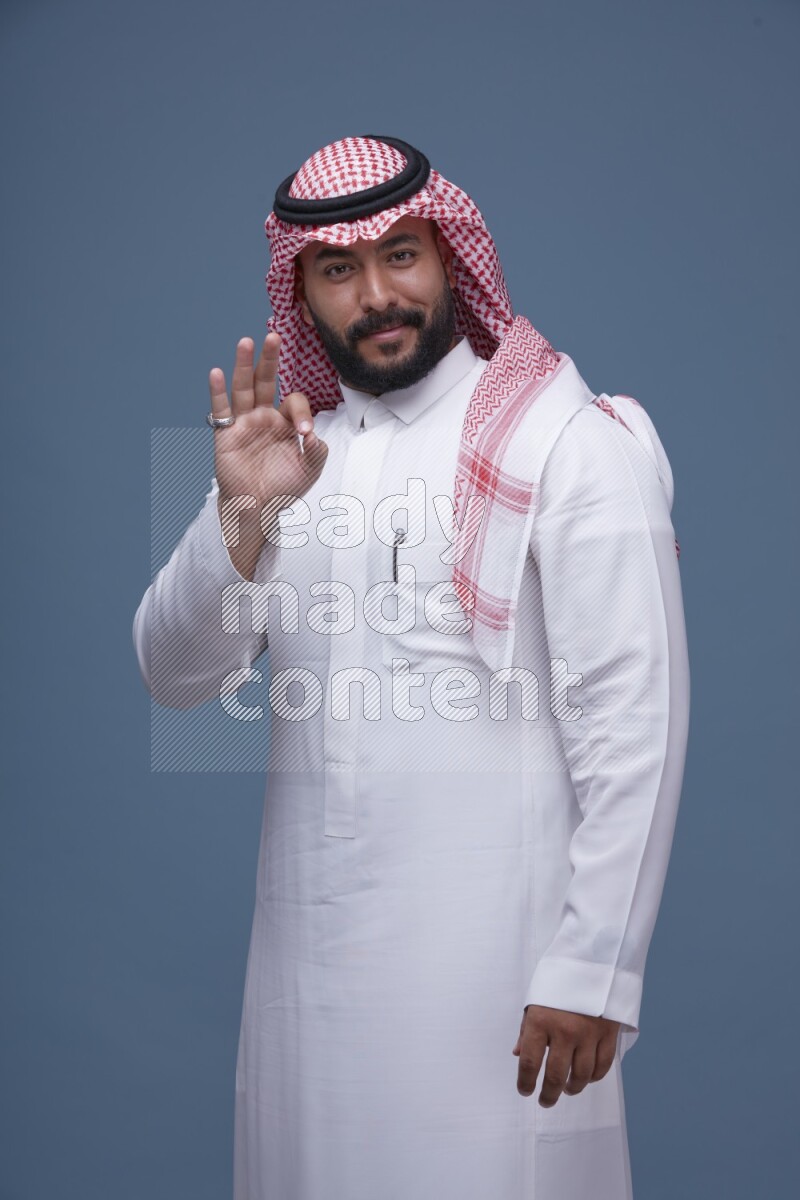 A Saudi man posing on blue background wearing Thob and Shomag