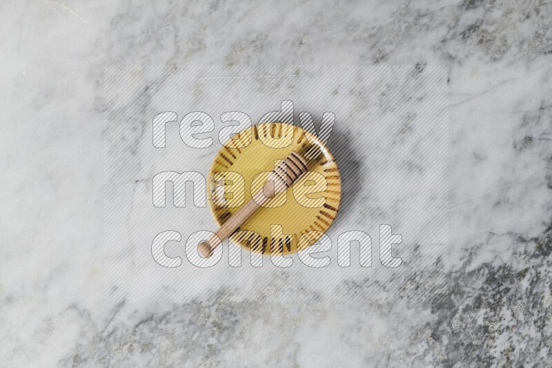 Multicolored pottery plate with wooden honey dipper in it on grey marble background