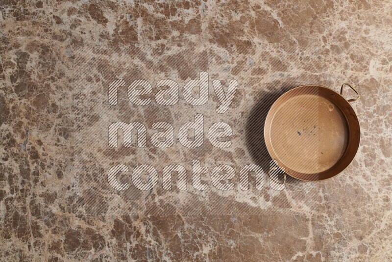 A small copper pan on beige marble background