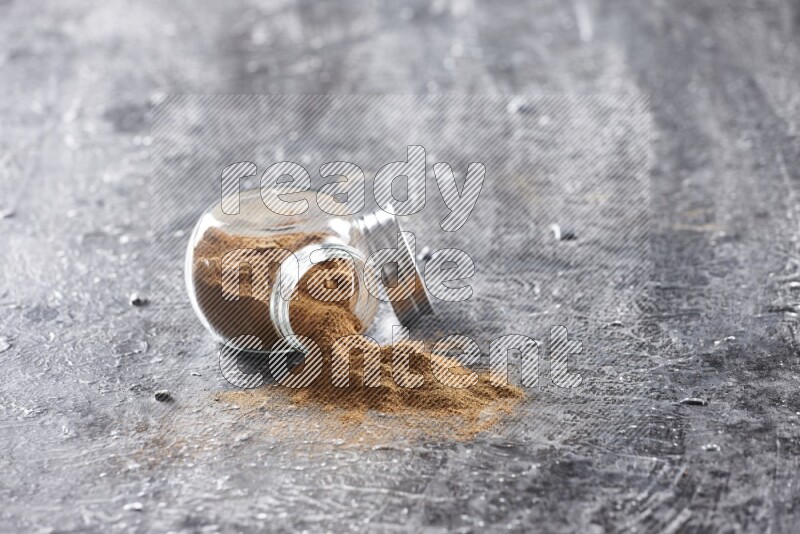Flipped herbal glass jar full of cinnamon powder on textured black background