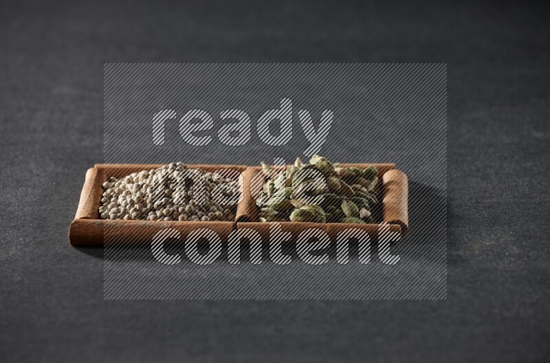 مربعان من أعواد القرفة ممتلئان بحبوب الفلفل الأبيض وحبوب الهيل علي خلفية سوداء