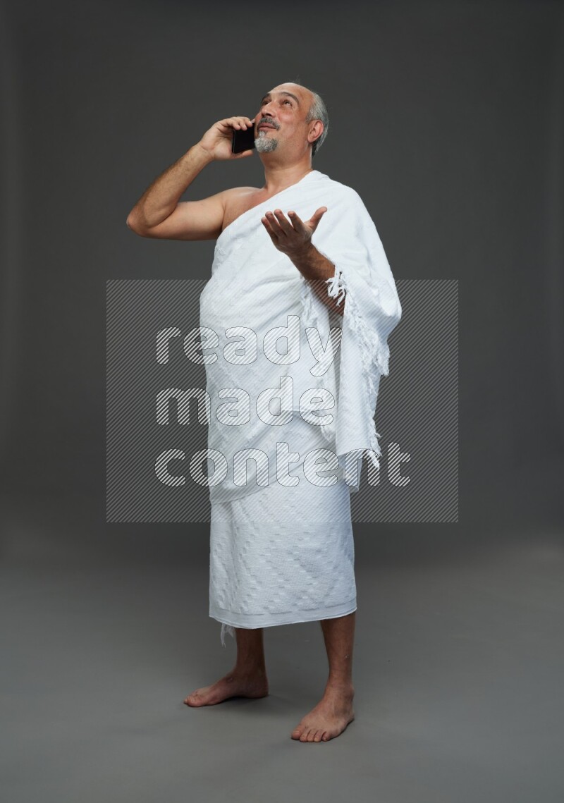 A man wearing Ehram Standing talking on phone on gray background