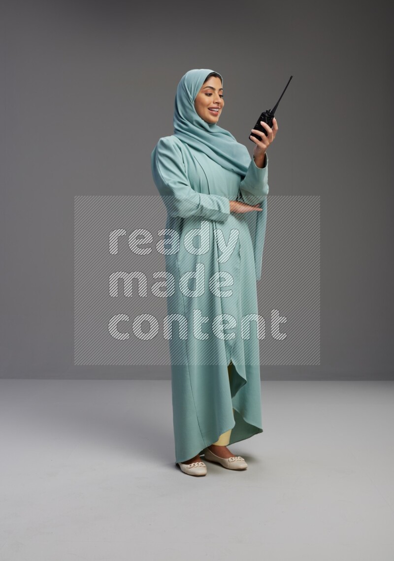 Saudi Woman wearing Abaya standing holding walkie-talkie on Gray background